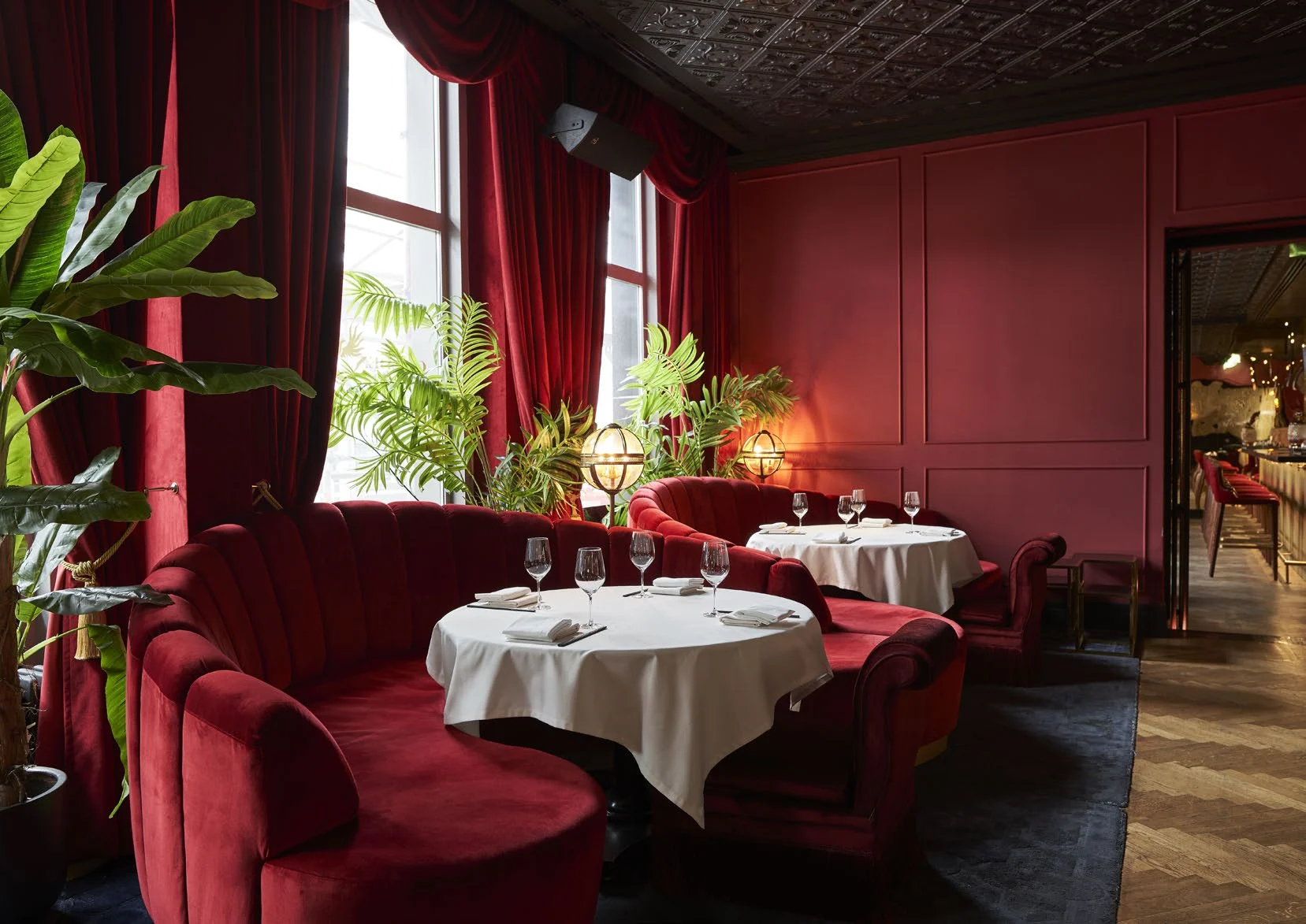 Cozy restaurant with red velvet seating, white tablecloths, and lush green plants.