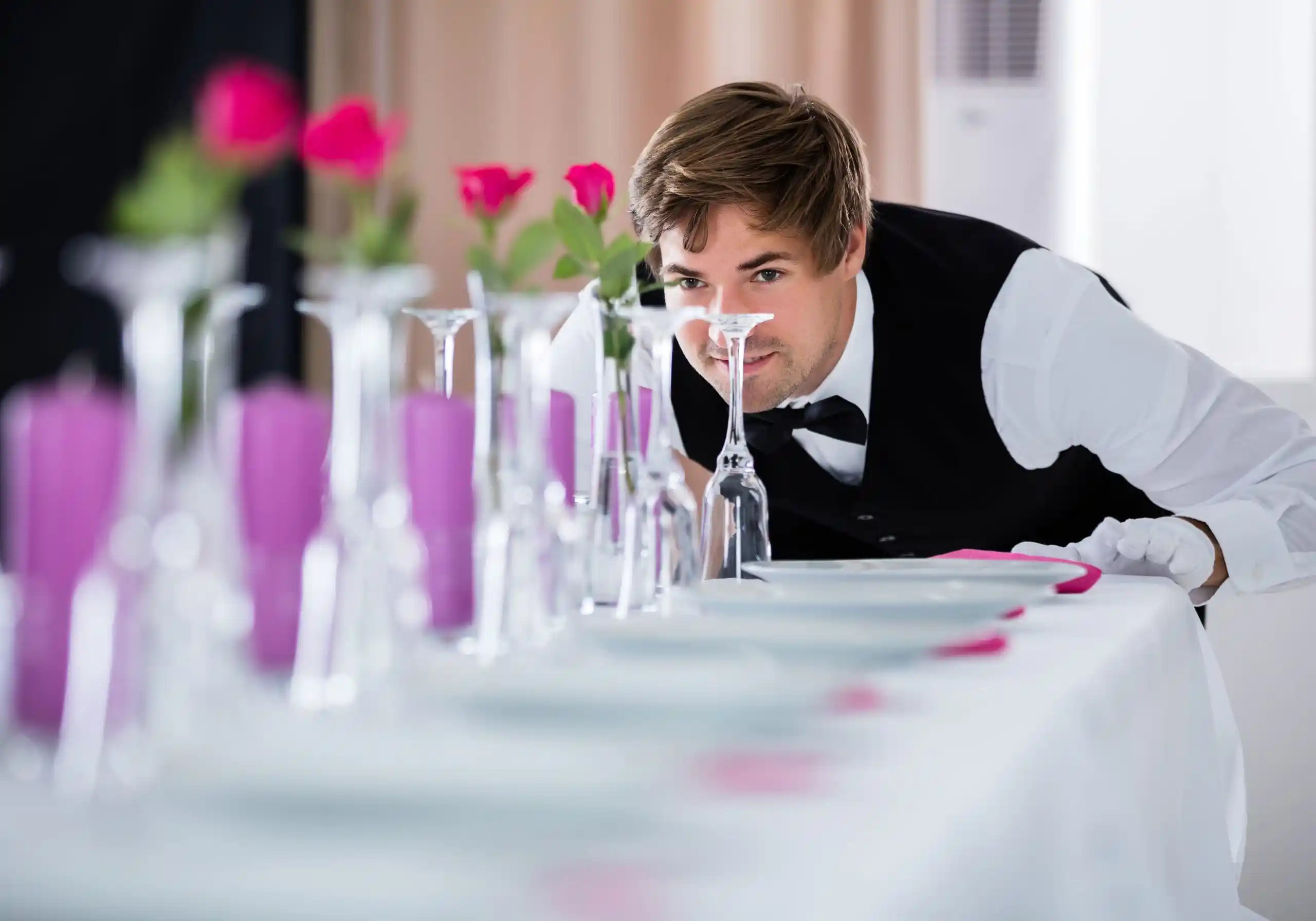 Waiter inspecting flower arrangements at event table for Ecorens.